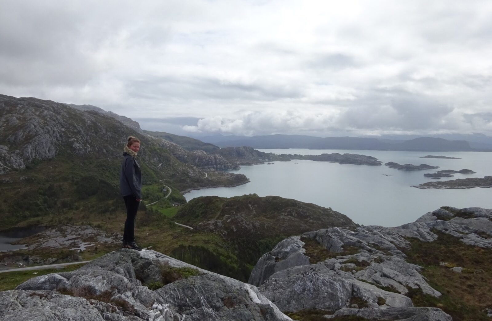 Bilde av en ung dame på toppen av et fjell med utsikt over havet