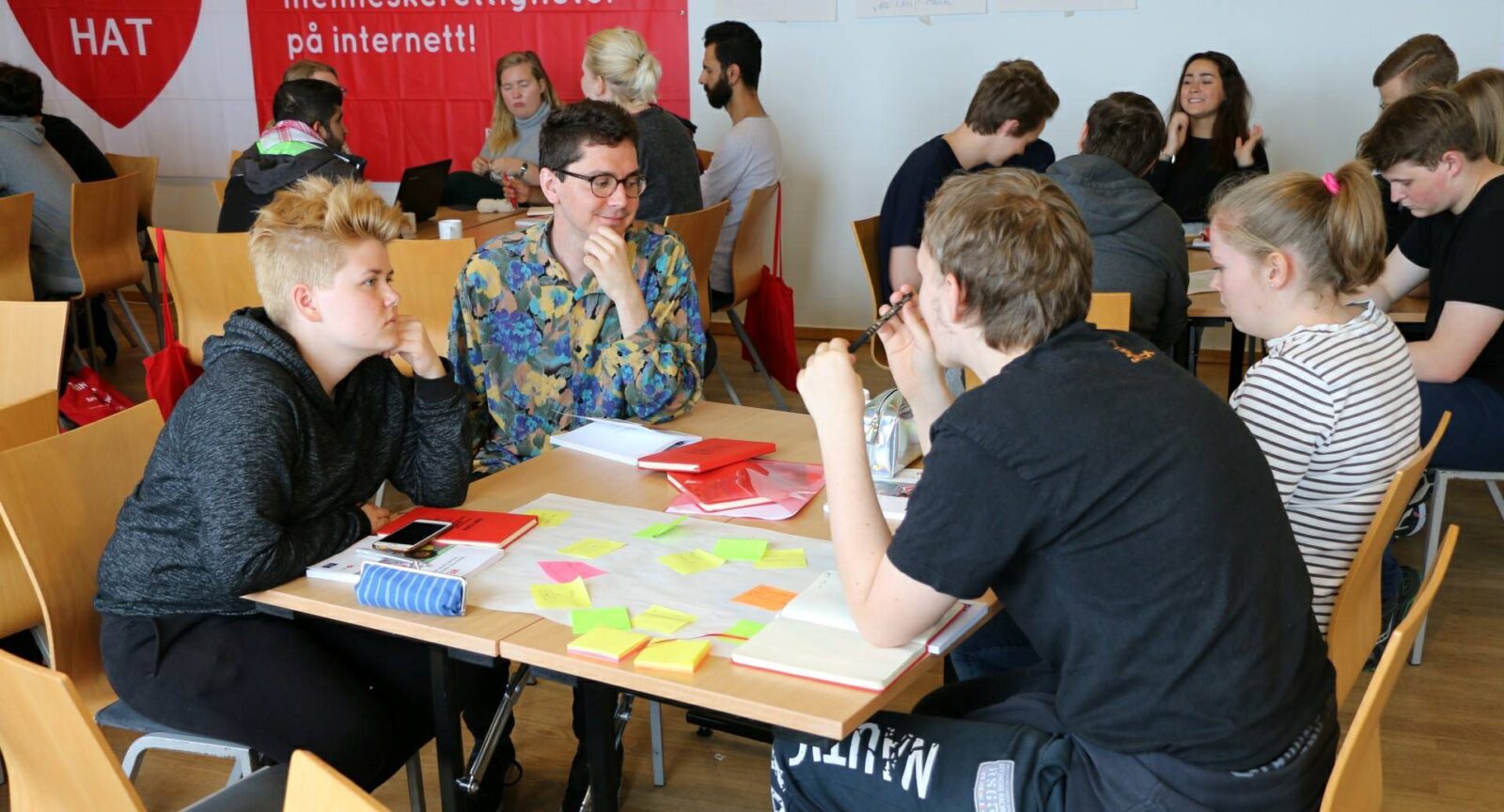 Ungdommer sitter rundt bord og diskuterer