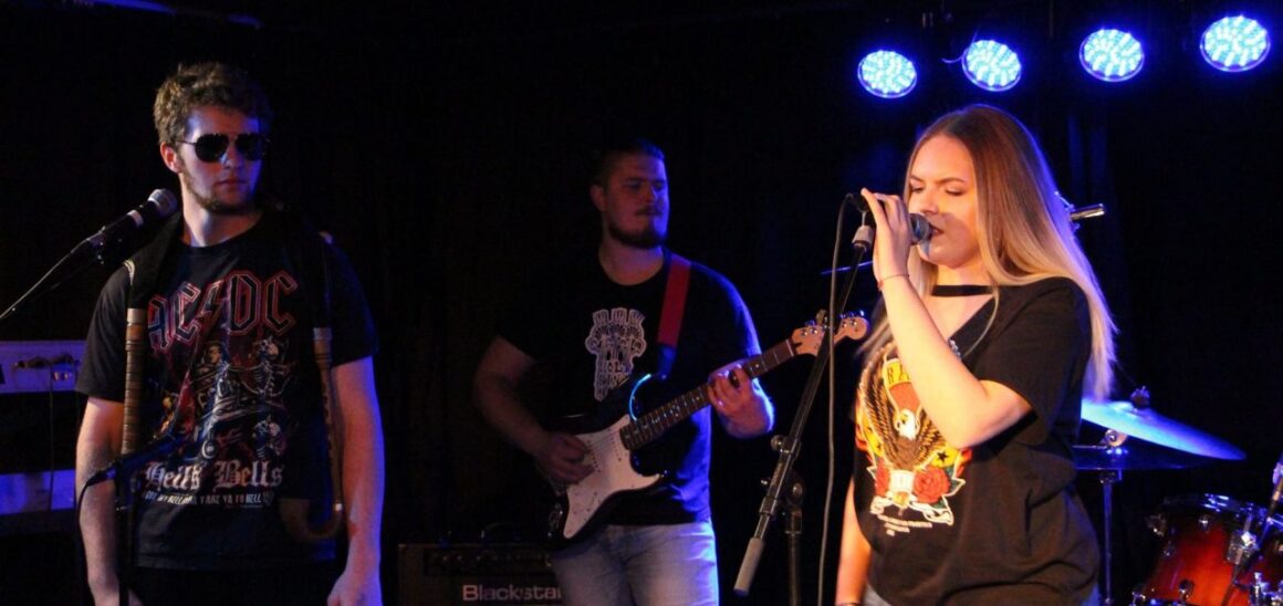 Tre ungdommer på en scene fremfører en rockesang