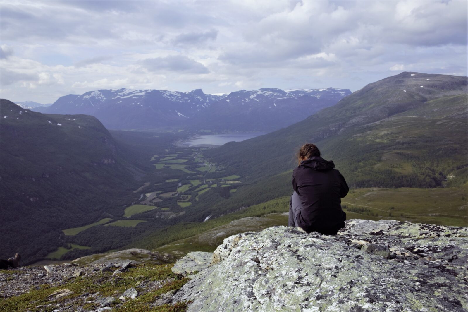 En ung kvinne sitter og ser utover nordnorsk natur