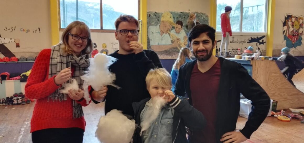 Tre unge voksne og et barn spiser sukkerspinn i en gymsal