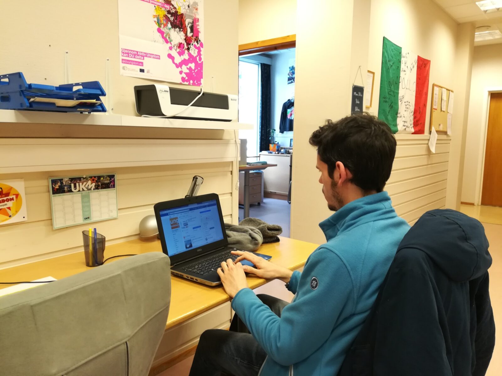 Bilde av en ung frivillig mann som sitter med ryggen til foran en laptop