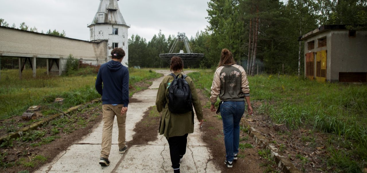 Tre personer går en vei i et område med falleferdige bygninger i Latvia
