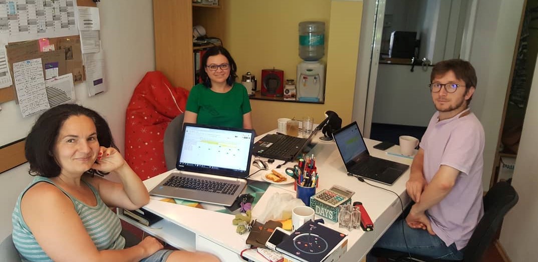 To kvinner og en mann sitter ved et bord med laptop foran seg