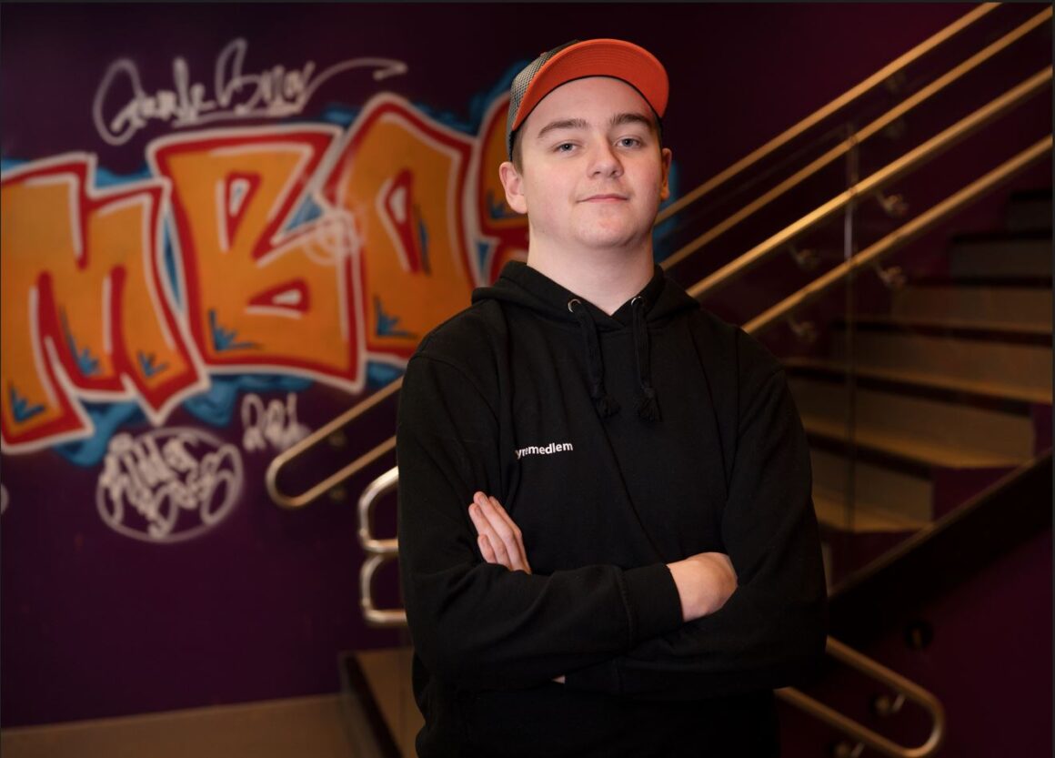 En ungdom med caps står foran en trapp med grafittimalt vegg