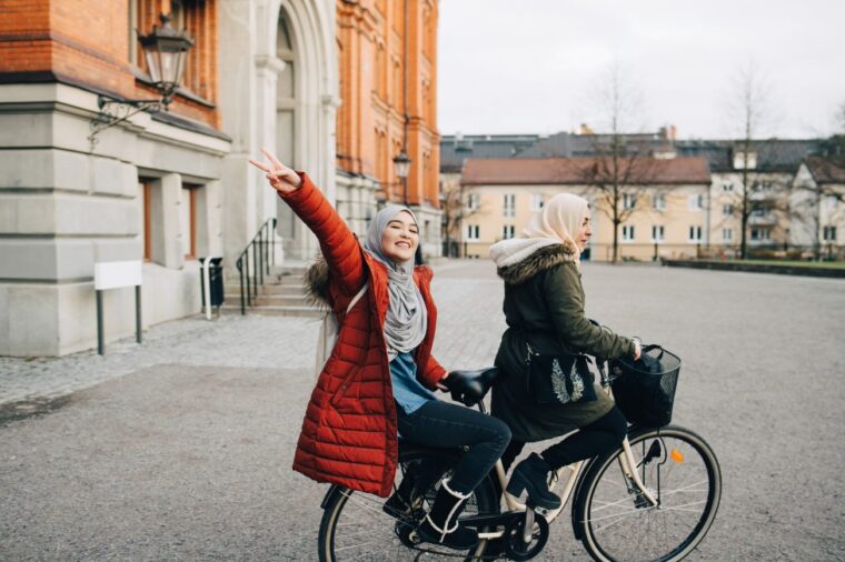 To unge kvinner sitter på en sykkel og vinker